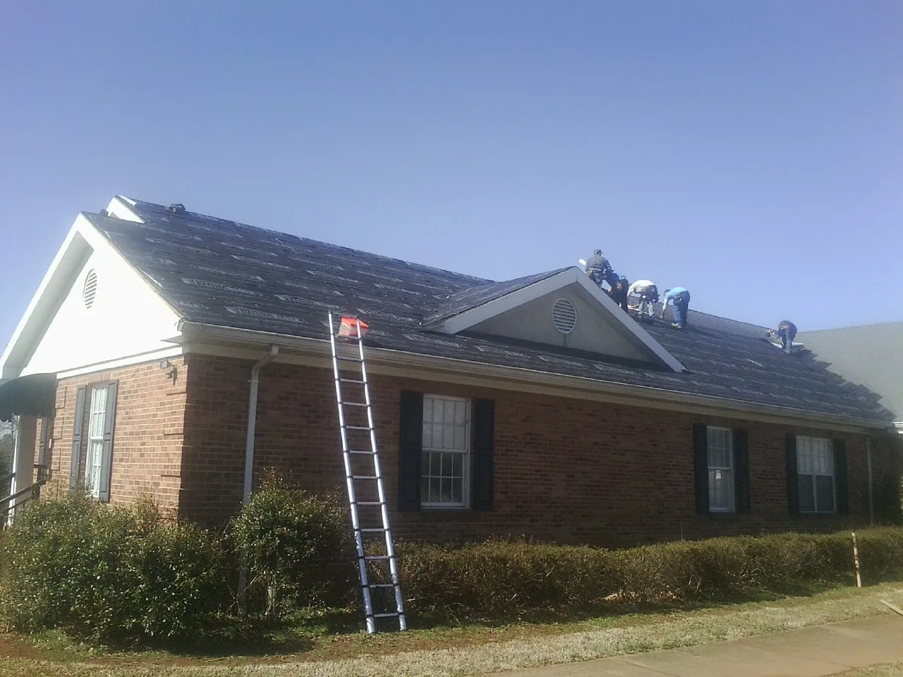 Crew tearing shingles off a brick ranch roof with a ladder set — Emergency Roof Repair work by our crew in Cordova